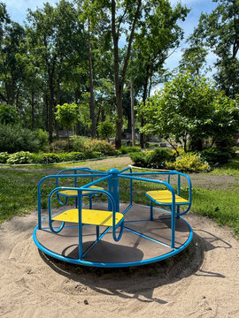Empty blue and yellow children's carousel on a playground in a green summer park.