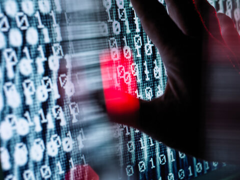 Close-up of hand touching computer screen with binary code