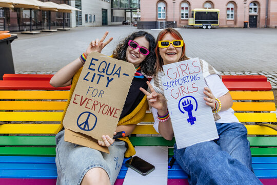 Activist holding equality and feminism sign sitting on rainbow bench