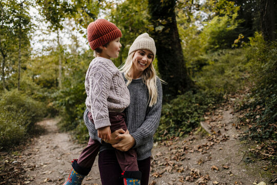 Mother holding son and walking in autumn forest smiling
