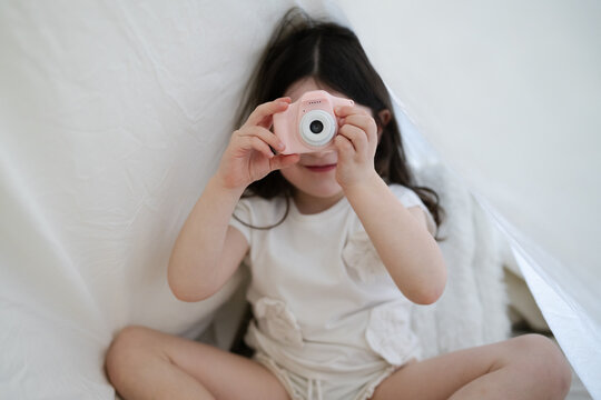 Playing with a pink toy camera inside a homemade blanket fort