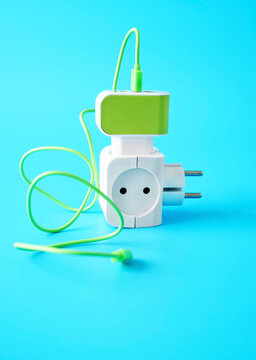 Green cable connected to plug adapter and electric outlet on blue background