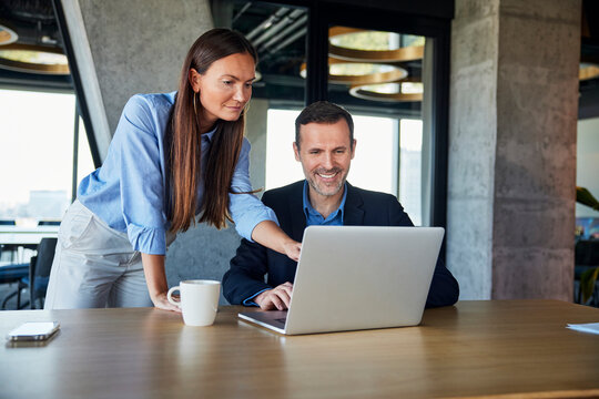 Businesswoman discussing with smiling colleague over laptop at desk