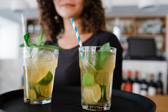 Young waitress with tray serving cocktail drinks at restaurant