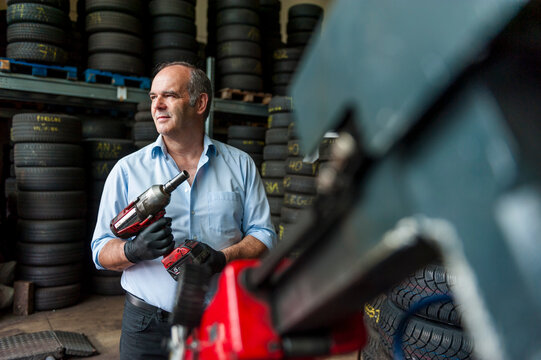 Senior entrepreneur holding impact wrench while looking away at tire store