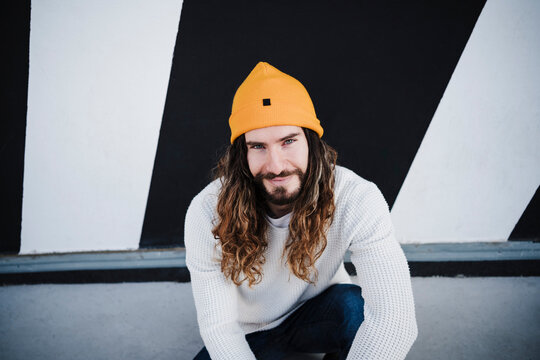 Smiling man with long hair sitting on footpath