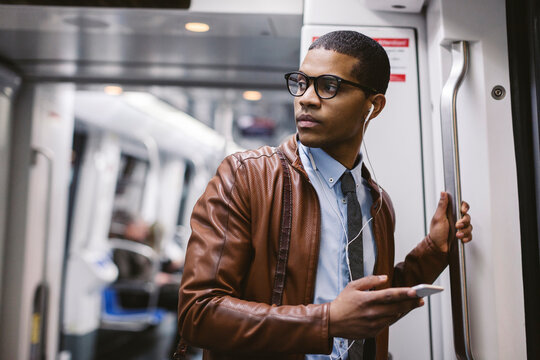 Businessman with smartphone and earphones hearing music on the subway train