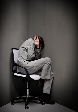 Businessman hiding in corner of room experiencing stress