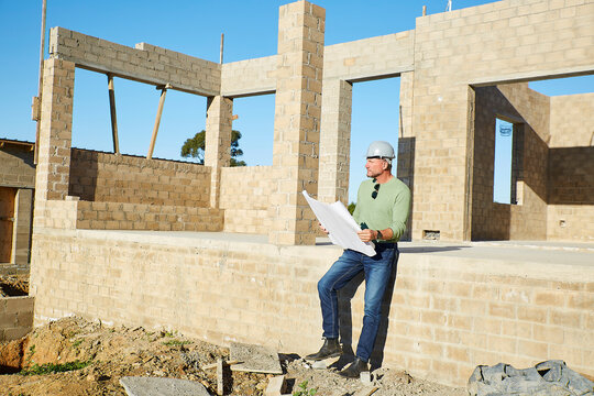 Builder sitting outdoors at construction site reviewing blueprint