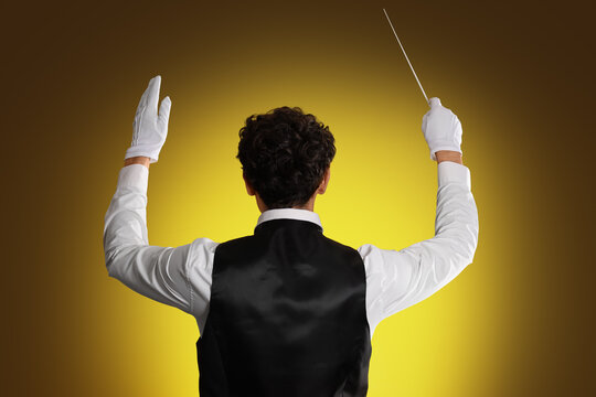 Young male conductor on dark yellow background, back view