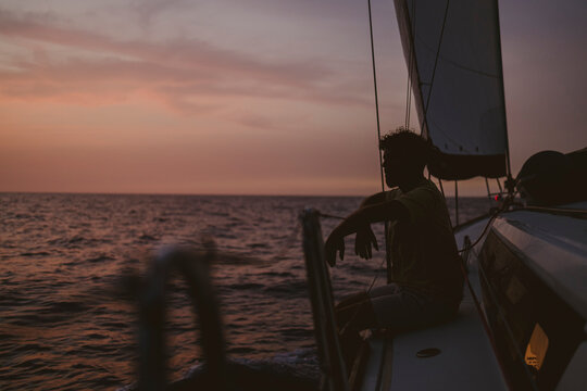 Silhouette sitting on sailboat deck looking at ocean during sunset