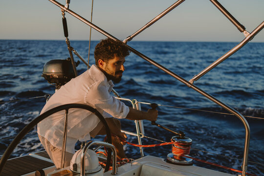 Sailor operating winch on sailboat during summer sunset