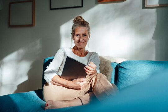 Smiling woman holding tablet PC on sofa in living room