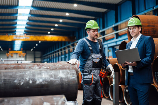 Male manager using laptop while standing by warehouse worker in factory