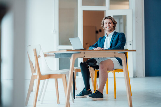 Smiling businessman sitting with laptop at desk in office