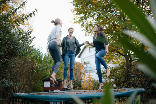 Happy mother with two teenage girls jumping on trampoline in garden in autumn