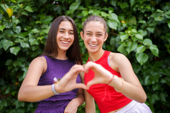 Friends making a heart shape with hands in a garden
