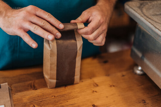 Close-up of man packing bag of coffee at shop counter