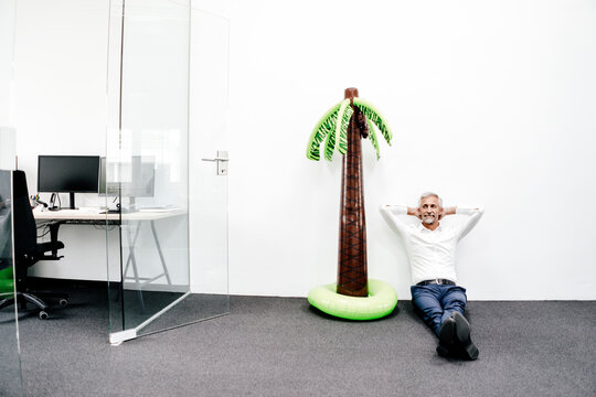 Smiling mature businessman sitting next to inflatable palm tree in office