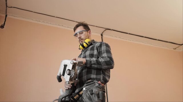 Electrician in safety glasses and ear protection examines wall chasing tool during construction equipment inspection
