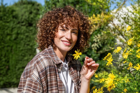 Smiling woman with curly hair holding a yellow flower in a spring garden