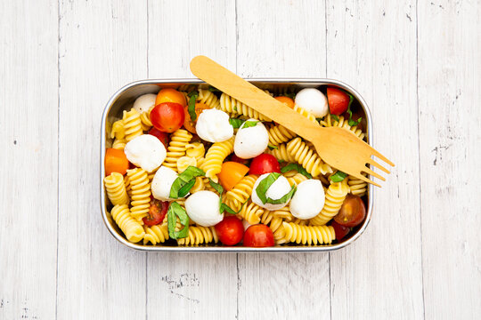 Healthy vegetarian pasta salad in a metal lunchbox on white wood