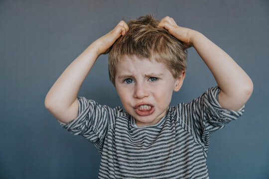 Frustrated boy scratching head against gray background