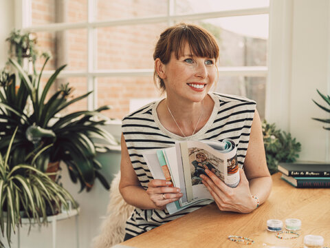 Smiling crafter holding magazine at table indoors