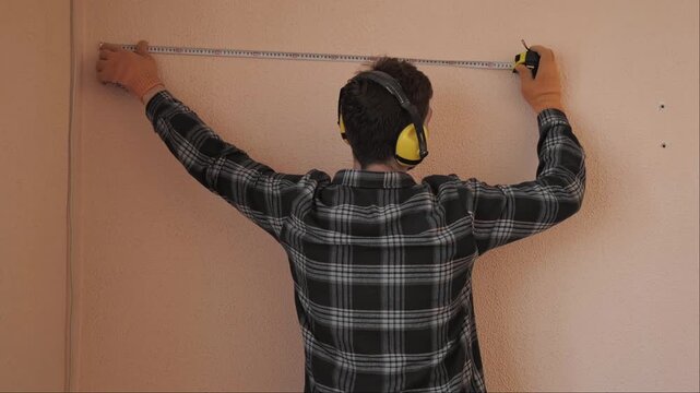 Repair specialist measures with tape preparing for electrical cable installation during indoor construction work