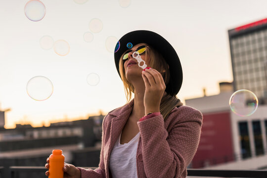 Young woman in the city blowing soap bubbles in the evening