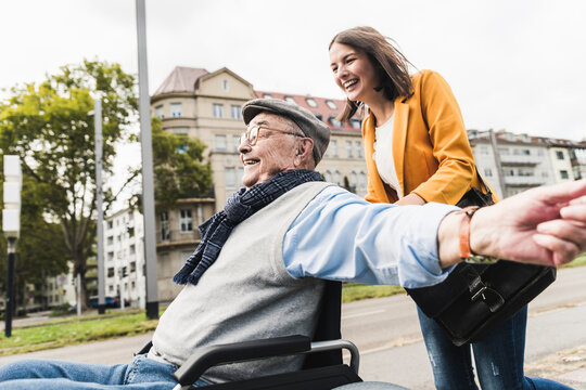 Laughing young woman pushing happy senior man in wheelchair
