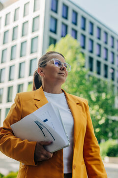 Confident corporate manager holding laptop and document outdoors