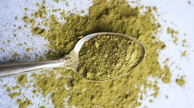 Spoon filled with matcha powder on textured surface