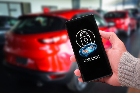 Hand holding a smartphone using a smart digital key application to unlock a modern red car remotely