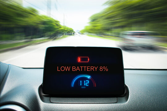Dashboard display of an electric vehicle showing a low battery warning sign while driving fast on a road with motion blur