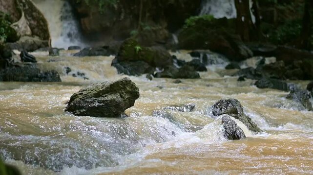 Slow motion shot of milky stream flowing from waterfall through the rocks in rain forest. Tranquil scene of muddy water flows from the cascade during rainy season. Tao Thong Waterfall. Phang Nga Provi