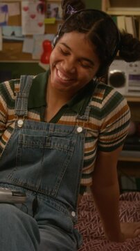 Vertical of black teenage girl wearing headphones listening and enjoying music from retro CD player and smiling in bedroom. Nostalgia marketing, youth lifestyle ads, or music app promos, vertical