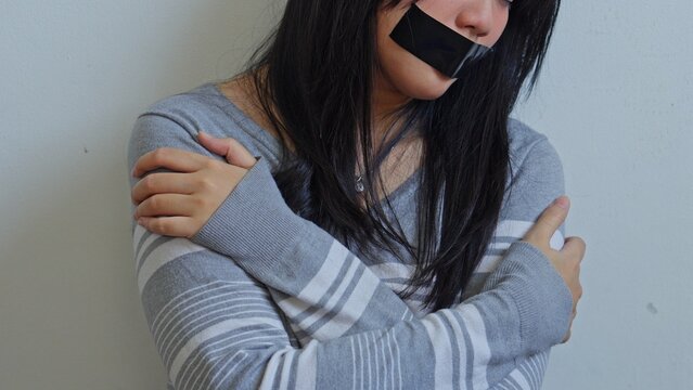 Terrified Young Woman With Tape Over Her Mouth Crosses Her Arms In Fear