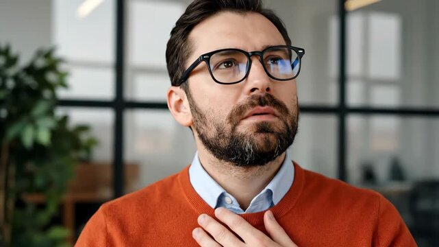 Man with beard and glasses experiencing discomfort or pain, possibly due to a health issue, touching his chest with a worried expression.