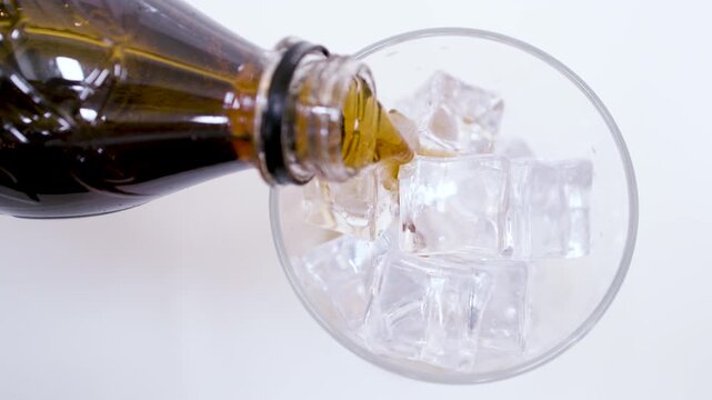 A dramatic close-up of cola exploding and splashing high out of a glass with ice cubes against a white background.