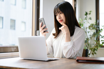 オフィスでノートパソコンとスマホを使って仕事をする日本人女性 © Yamatatsu
