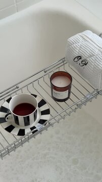Metal bathtub caddy tray with a candle and a striped coffee cup.