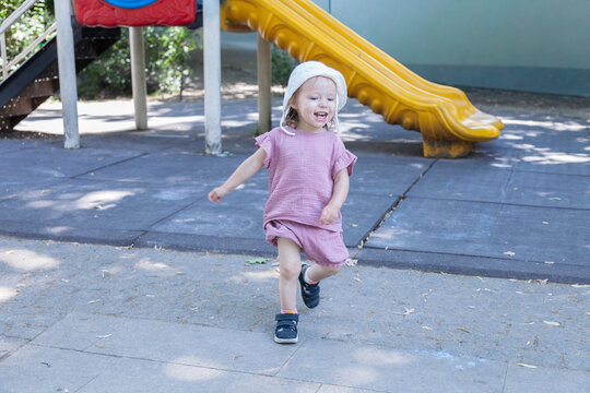 Smiling toddler girl running in front of a playground slide. Outdoor activity supports healthy growth curiosity and active learning.