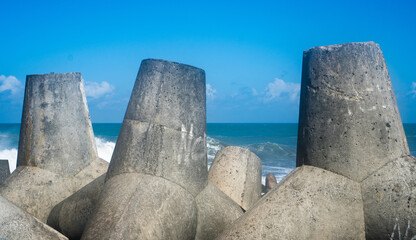 Concrete wave breaker structure on the shoreline with blue sea and sky. Coastal defense, marine construction, and environmental protection themes. © ANTONIUS