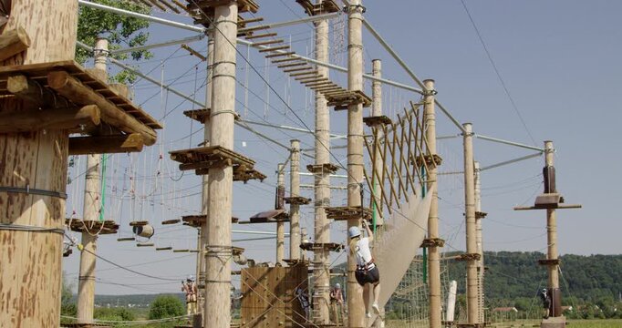 A person traversing an obstacle course on a wooden ropes course structure outdoors