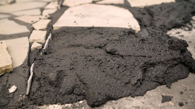 Black asphalt patch on cracked stone pavement