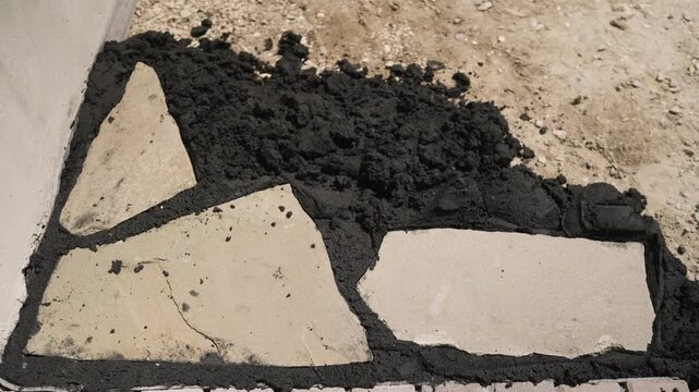 Close up of fresh black asphalt filling gap between light stone tiles. Rough texture, uneven edges, natural daylight. Urban repair scene. Neutral tones with dark contrast