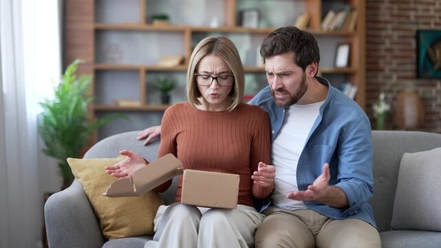 Disappointed married couple received a parcel with wrong product after opening box sitting on couch at home. Husband and wife are unhappy with shopping in online store. Service issue or damaged item