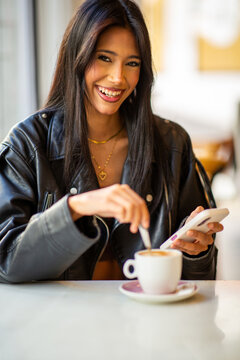 Smiling woman using smartphone and drinking coffee in cafe