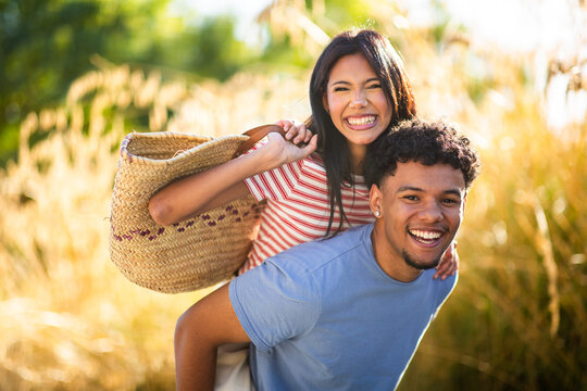 Smiling young couple enjoying piggyback ride in sunny golden field